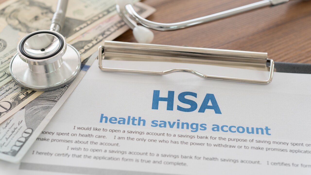 A clipboard with a paper reading "HSA: Health savings account" is sitting on a table next to a $50 and $100 bill and a stethoscope.