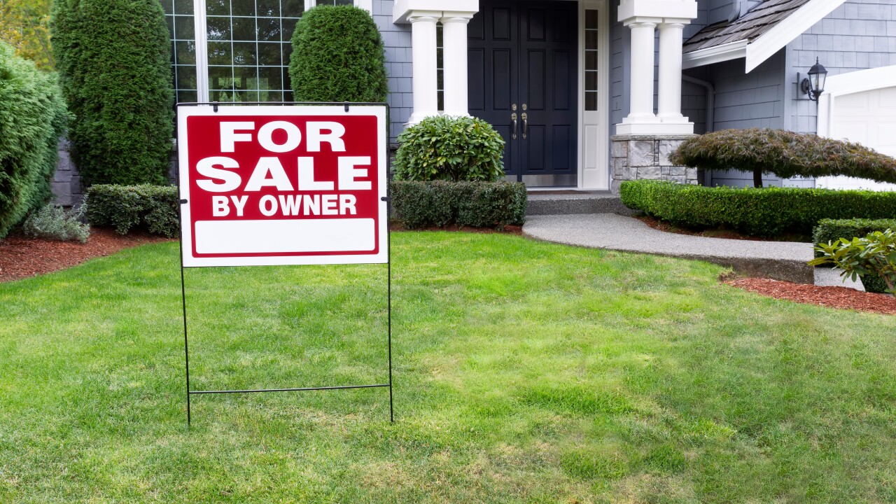 A "For Sale" sign in front of a large house