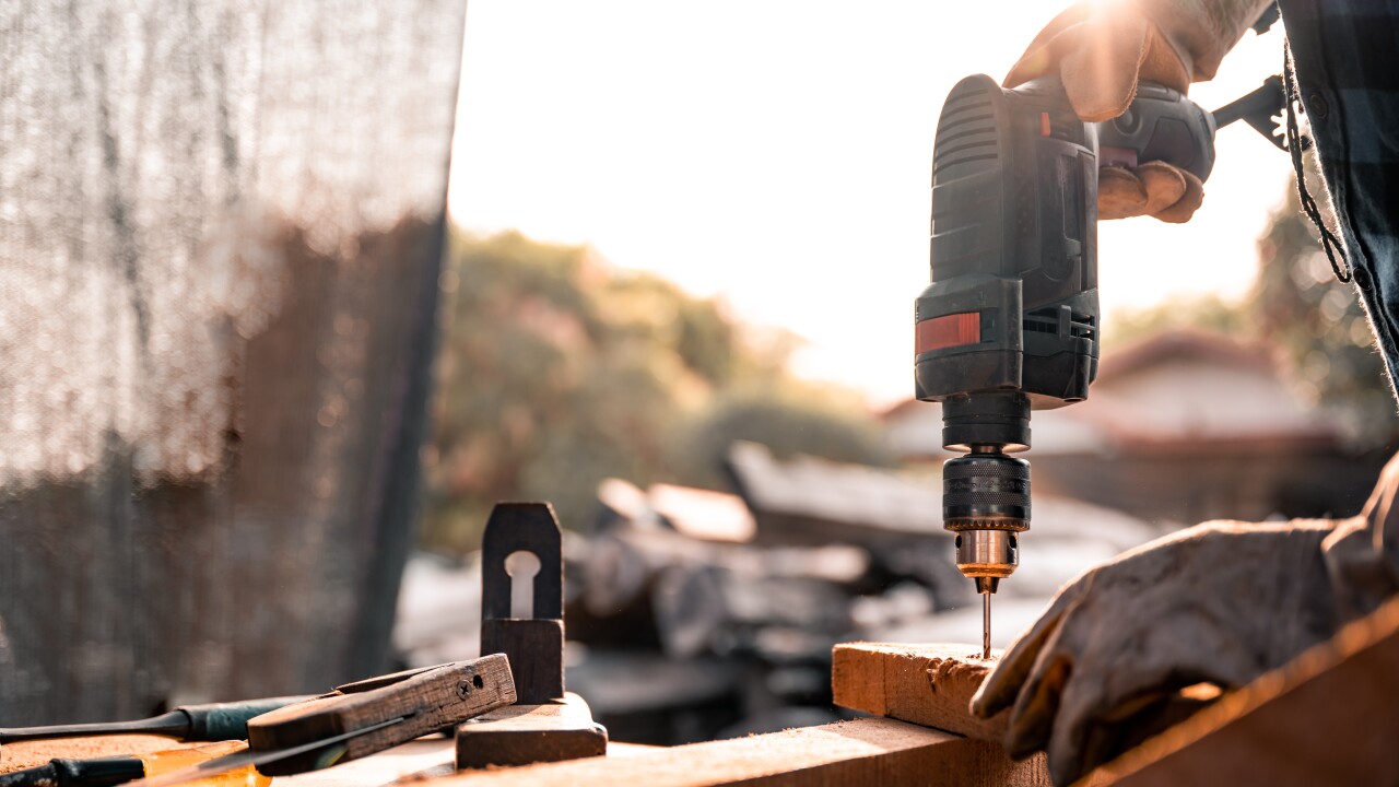 A construction worker drills a nail into a piece of wood at a building site