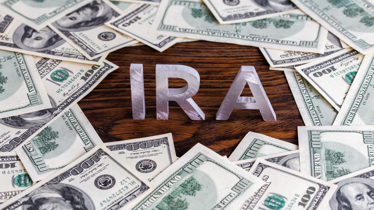 Silver block letters reading 'IRA' sit on a table surrounded by $100 bills