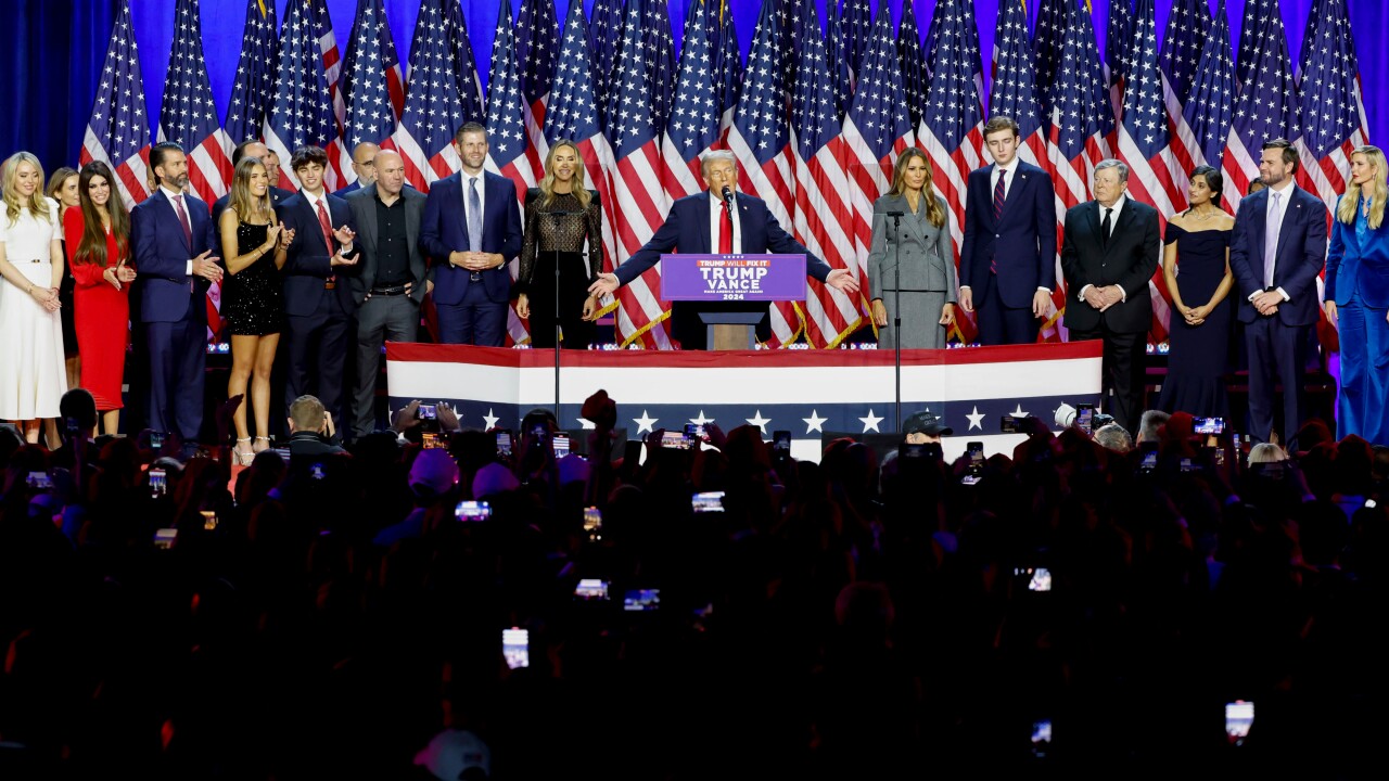 Donald Trump (center) speaking before a crowd on the night of Nov. 6. A series of American flags are in the background.