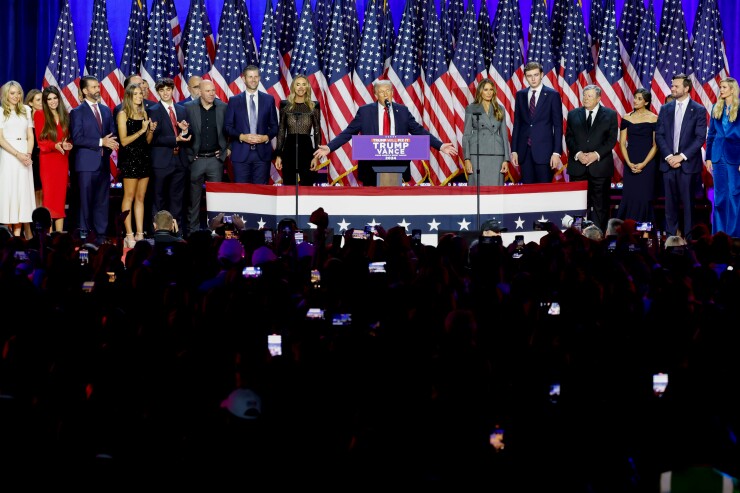 Donald Trump (center) speaking before a crowd on the night of Nov. 6. A series of American flags are in the background.