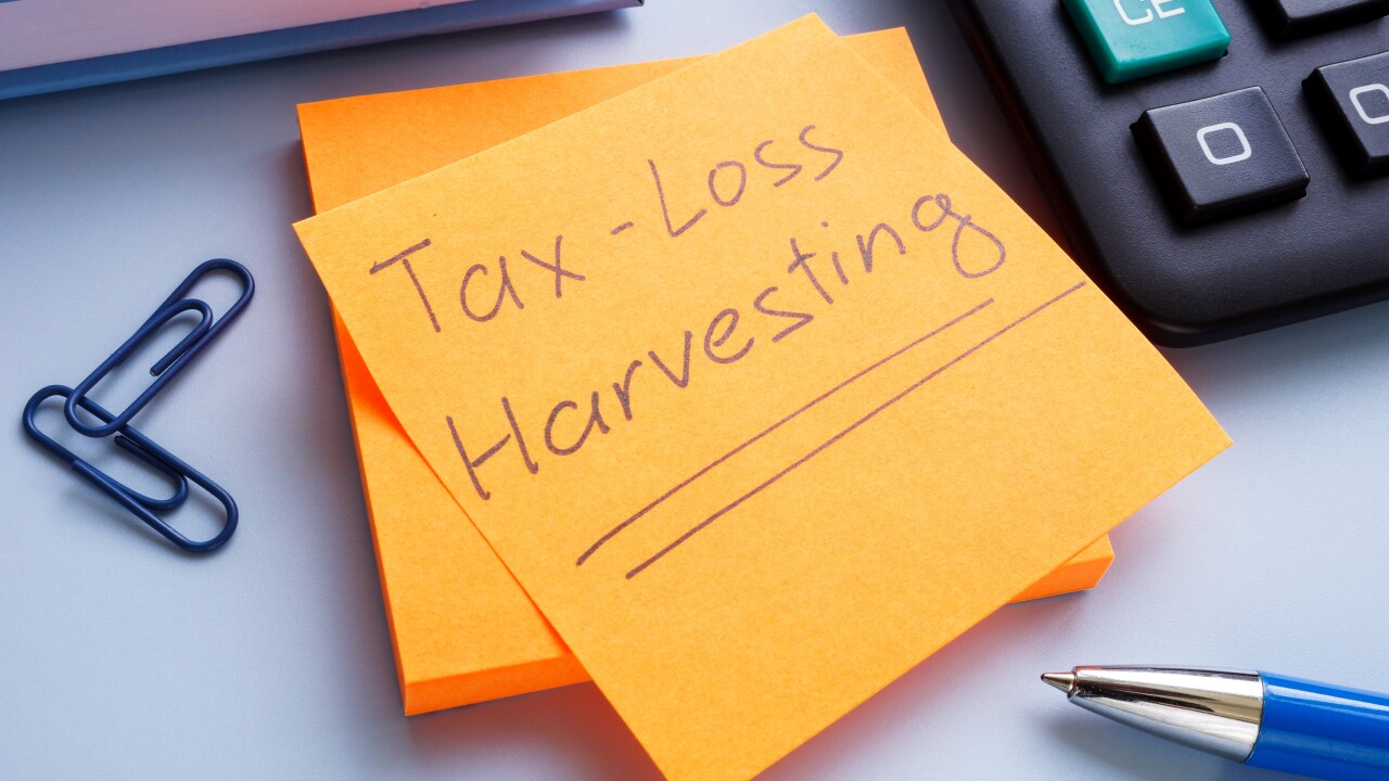 An orange post-it note reads 'Tax-loss harvesting' with the words underlined on top of a notepad sitting next to a pen, paper clips and a calculator on a desk