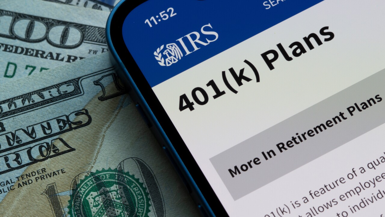 A smartphone with an IRS page explaining 401(k) plans sits on $100 bills